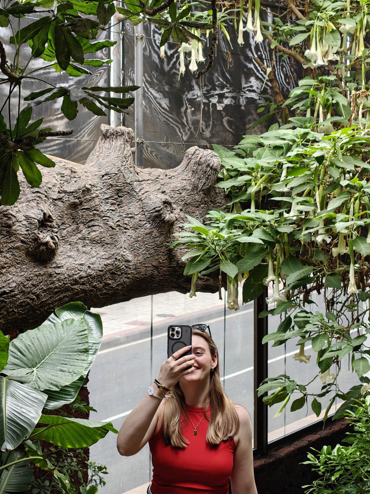 Liv macht ein Spiegel-Selfie zwischen tropischen Pflanzen mit weißen Blütenkelchen