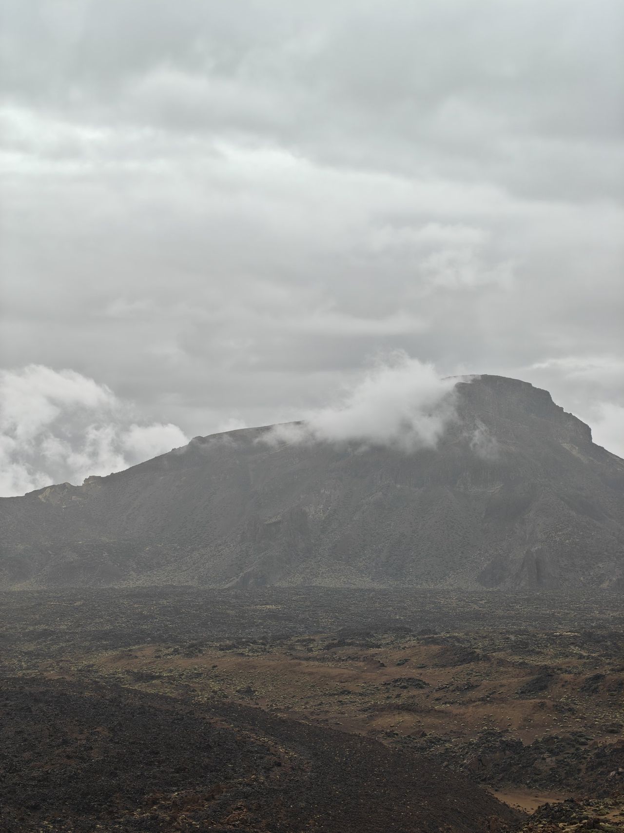 Ein Berg, um dessen Gipfel sich eine Wolke legt, davor Lavafelder